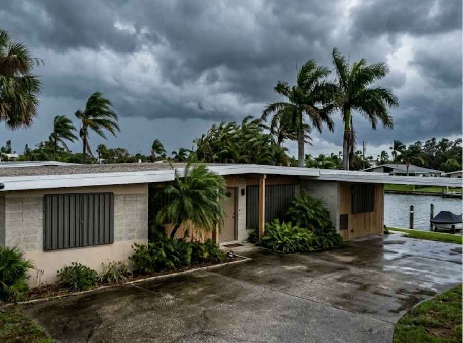 Mid-century Florida home along a canal with closed storm shutters under dark tropical storm clouds.